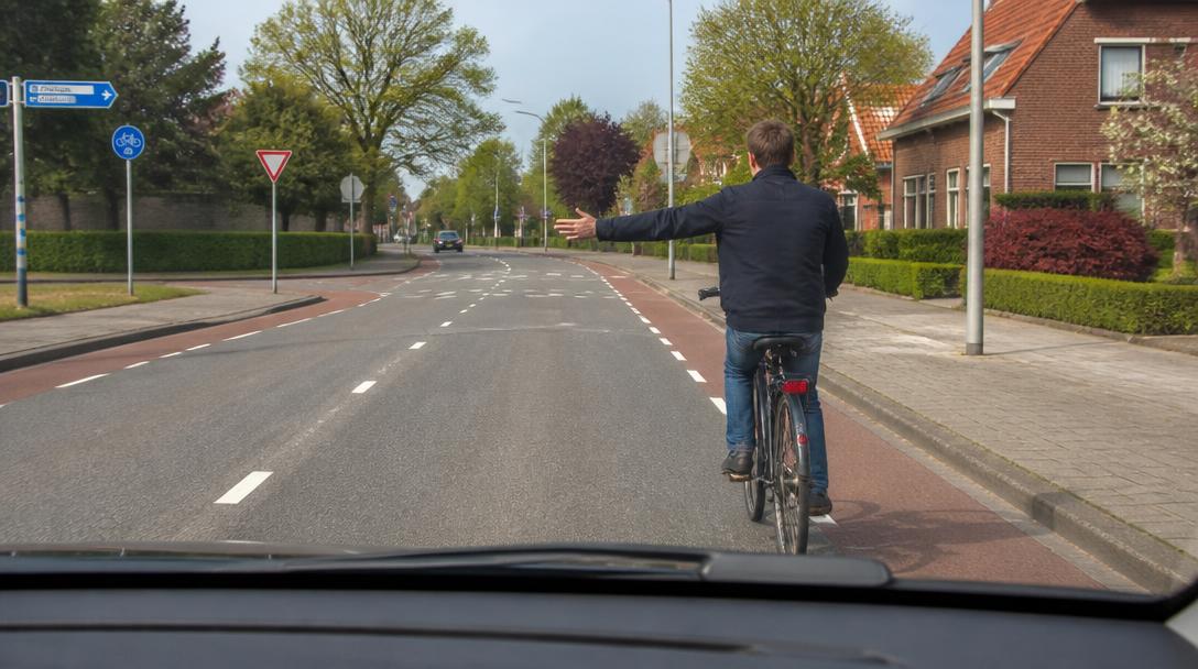 Fietser geeft met gestrekte linkerarm aan dat hij linksaf gaat