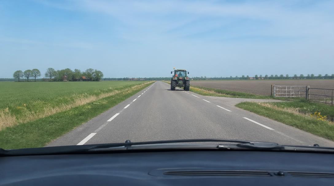 Langzaam rijdende tractor met zwaailicht op een buitenweg