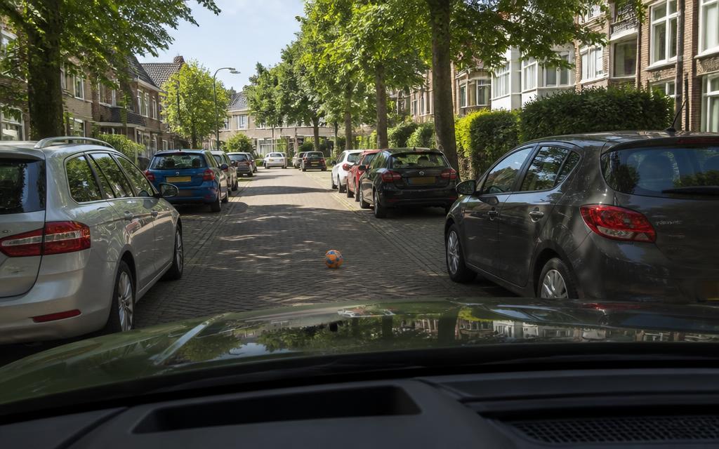Bal rolt tussen geparkeerde auto's de rijbaan op